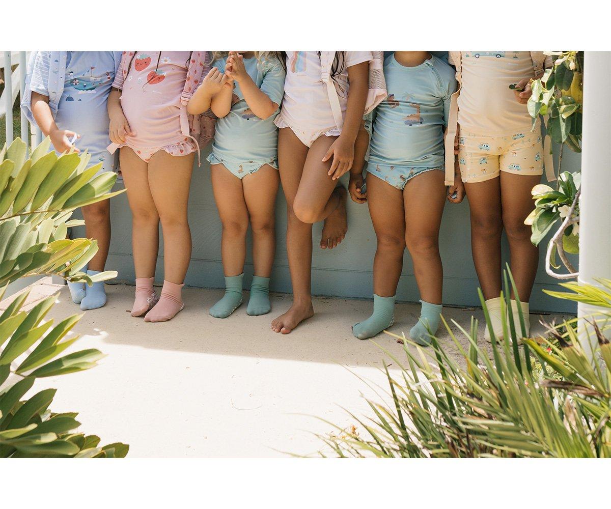 Crianças com roupas de banho coloridas e meias em tons pastel ao ar livre