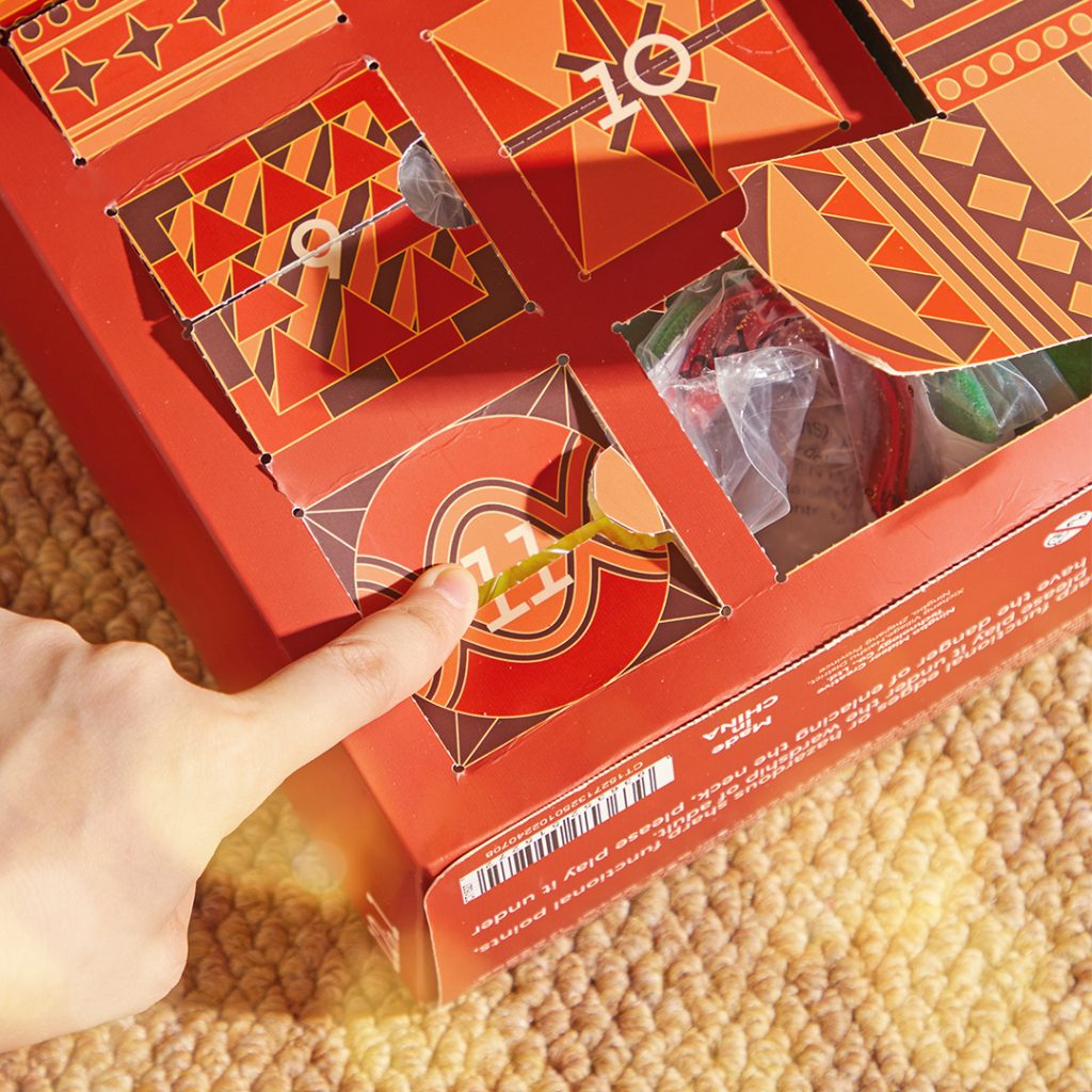 Caixa vermelha com portas numeradas e design geométrico, mão a abrir porta 11