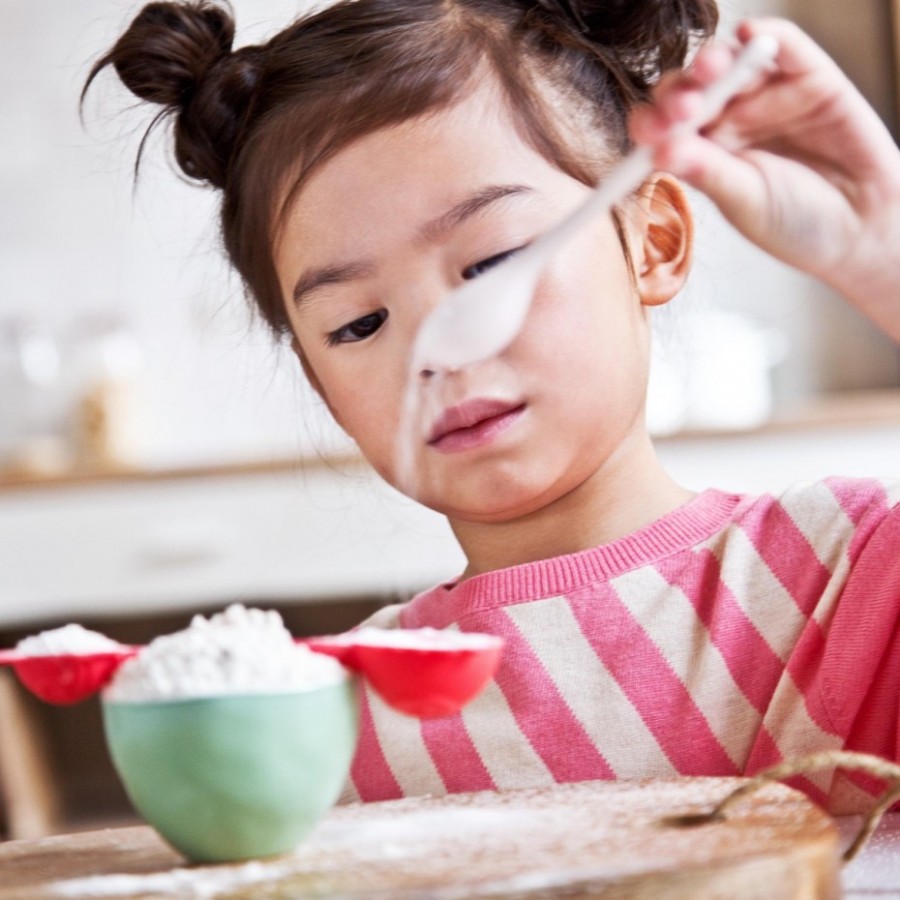Menina a mexer farinha branca numa tigela verde numa cozinha