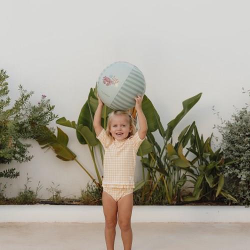 Criança com fato de banho e bola azul clara em ambiente exterior com plantas
