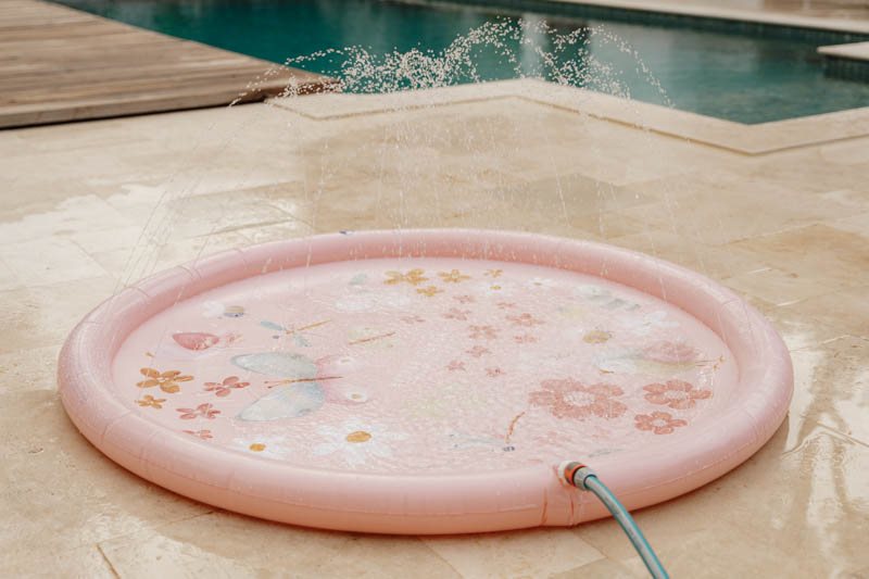 Piscina insuflável rosa com estampado de borboletas e flores a jorrar água.
