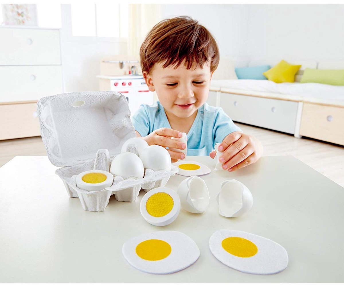 Brinquedo de ovos falsos em caixa de cartão com menino a brincar numa mesa branca