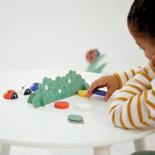 Brinquedo de madeira colorido com joaninhas e arbustos sobre mesa branca