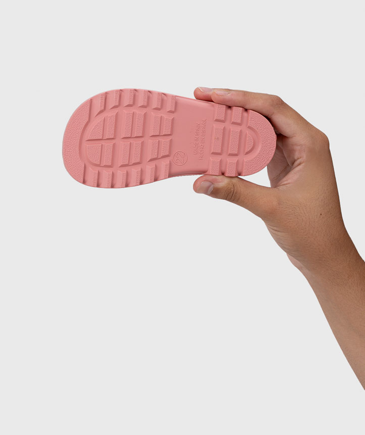 Sola de chinelo rosa com padrão antiderrapante e números, segurada por uma mão