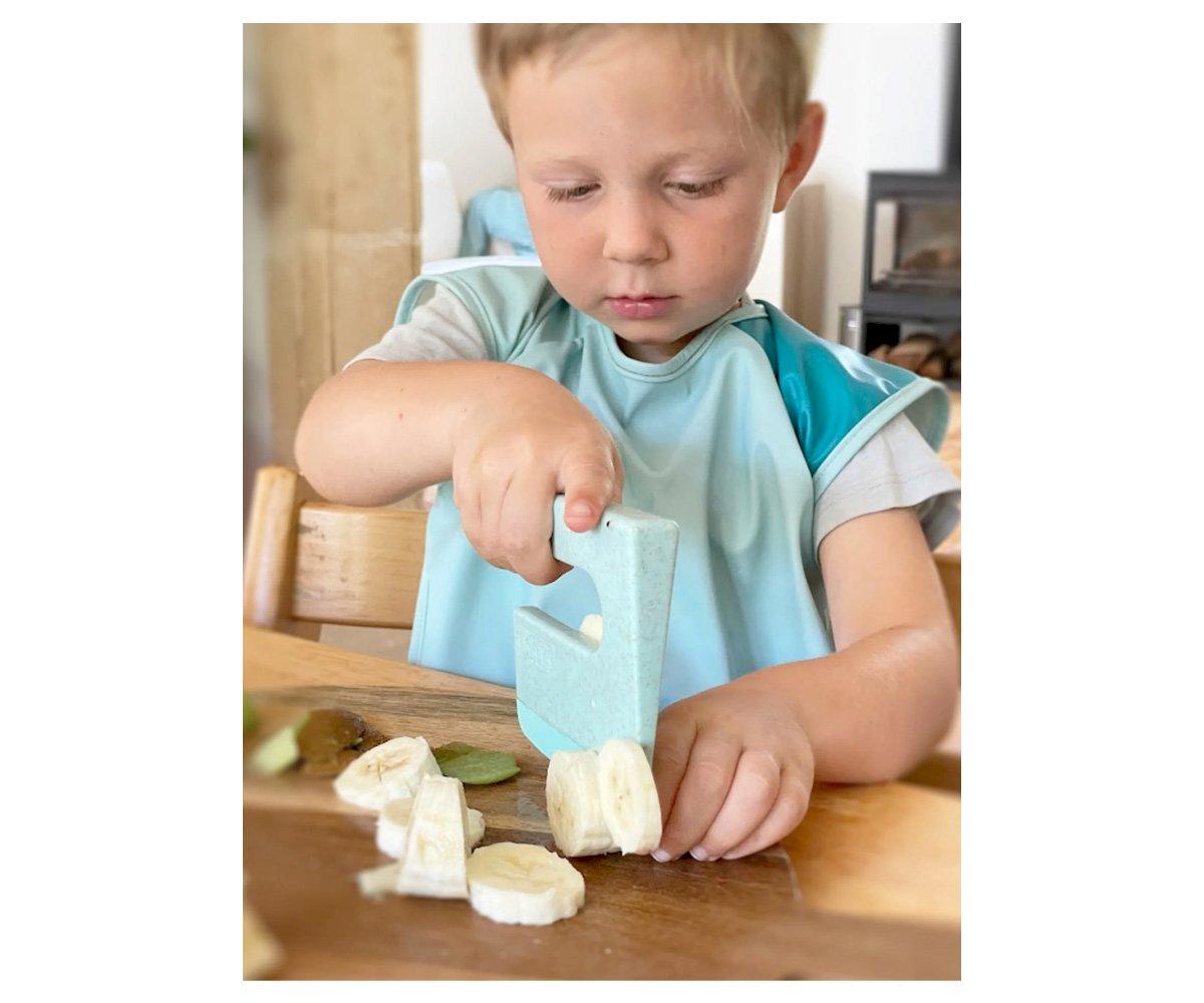 Criança fatiando banana com brinquedo cortador azul claro