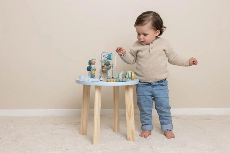 Criança pequena a brincar com brinquedo educativo de madeira colorida sobre mesa pequena