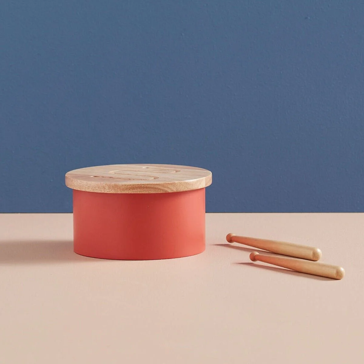 Tambor infantil vermelho com tampa de madeira e duas baquetas ao lado