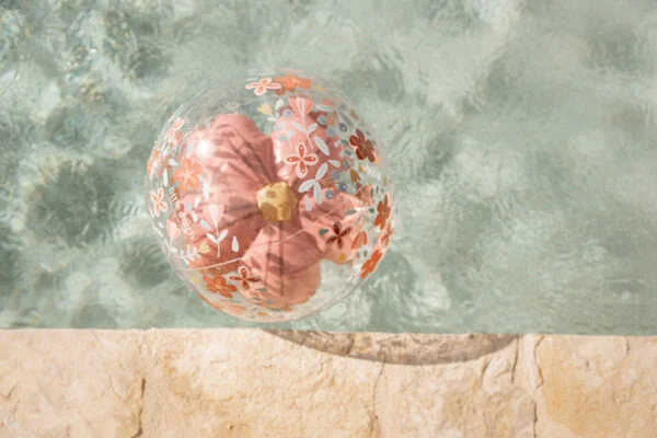Bola de praia transparente com flores cor-de-rosa e vermelhas a flutuar na água de uma piscina
