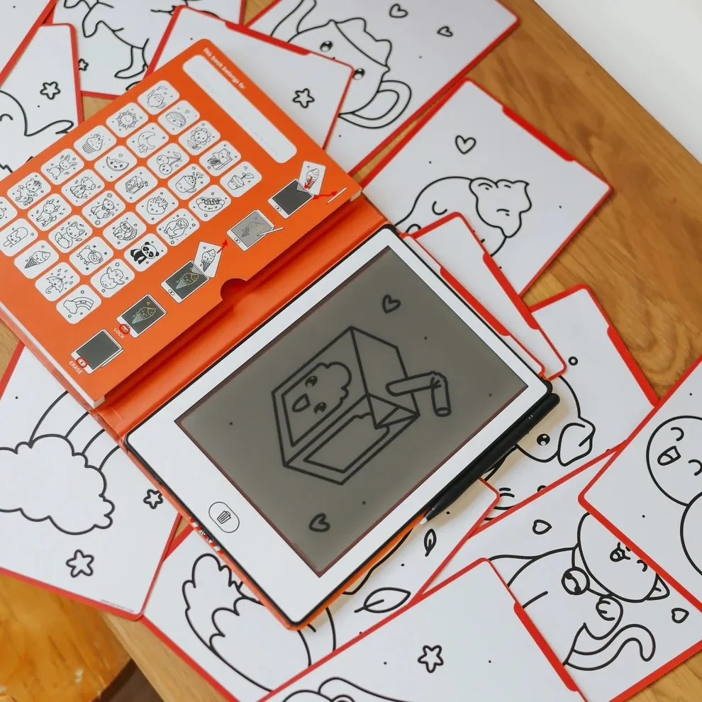 Tablet branco com capa laranja e cartas de desenhos em preto e branco com bordas vermelhas em superfície de madeira.