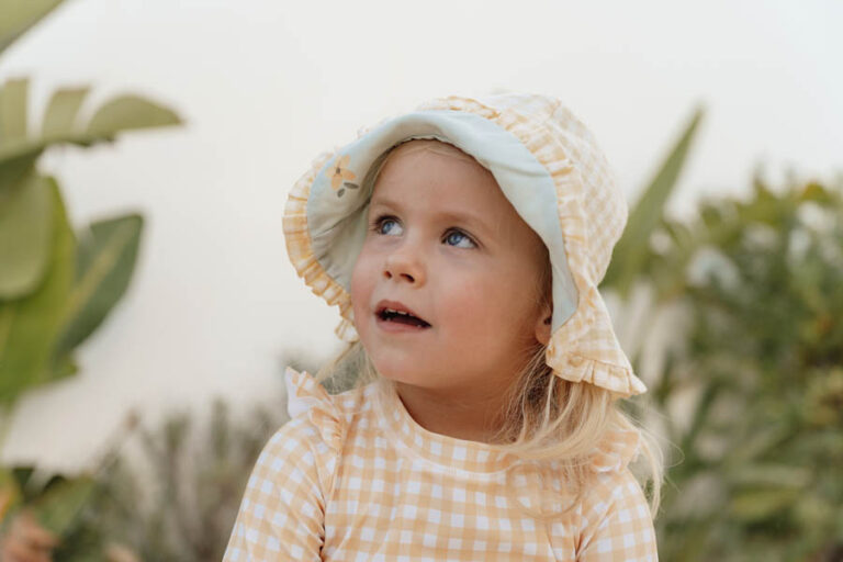 Menina pequena com chapéu e roupa quadriculados bege e branco ao ar livre