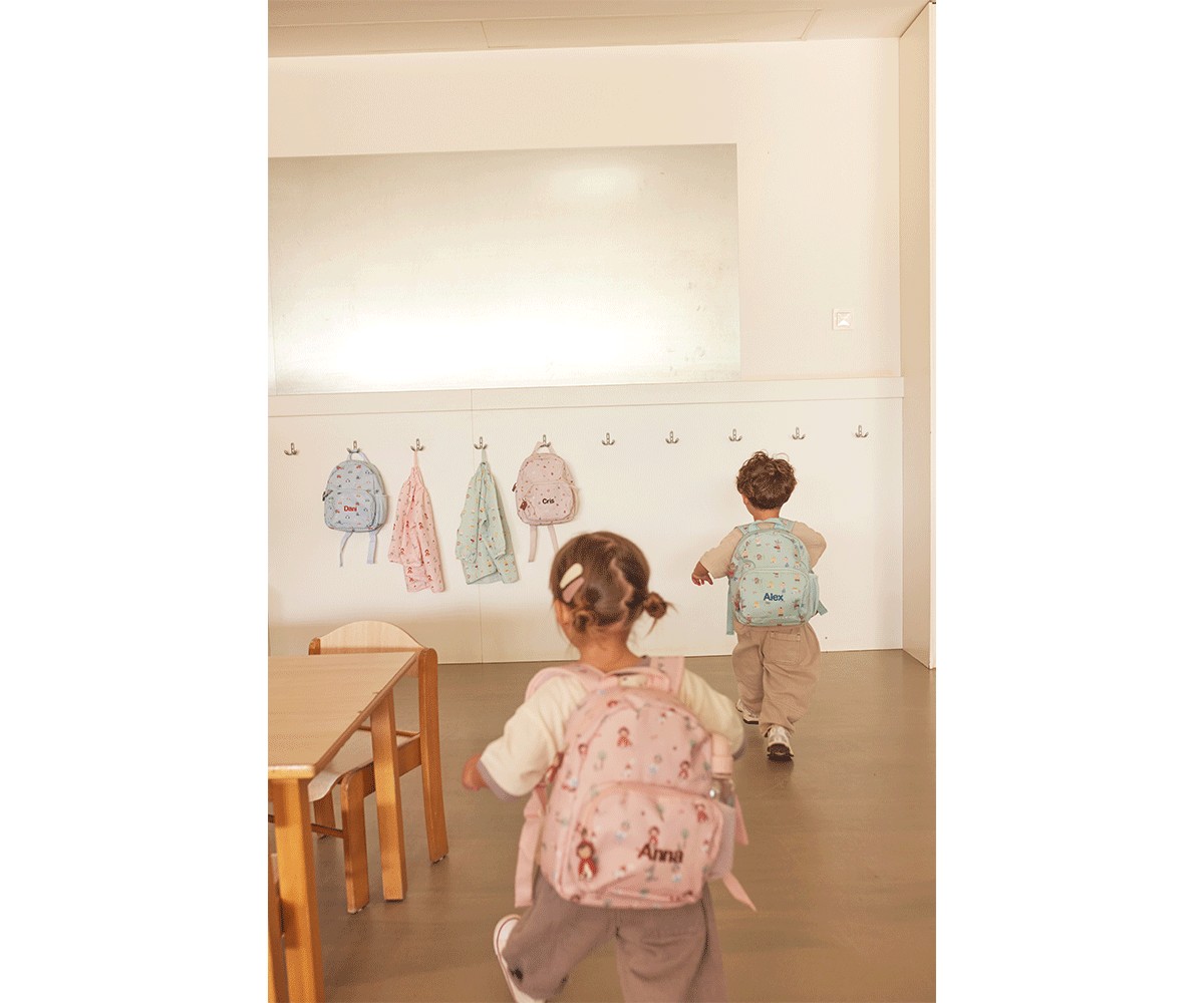 Crianças com mochilas cor-de-rosa e azul numa sala com cabides na parede