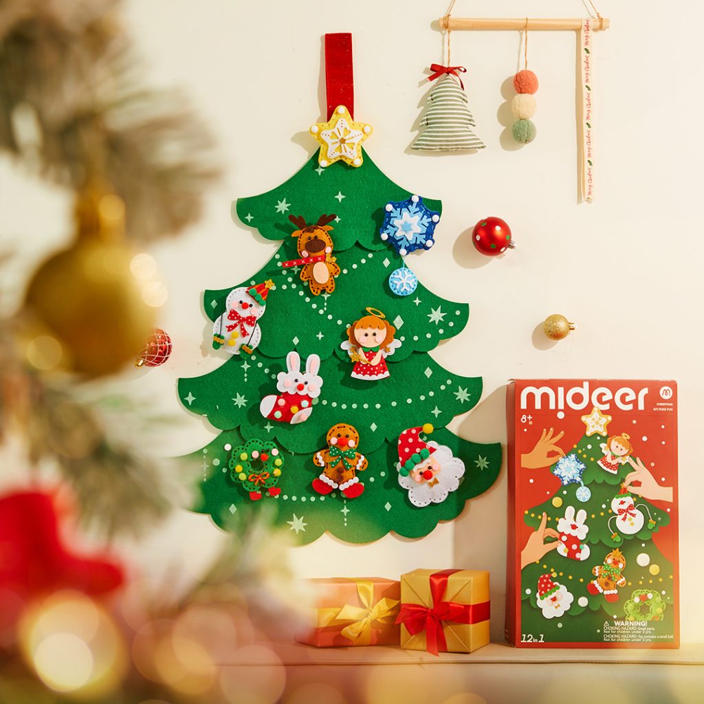 Árvore de Natal de feltro verde com enfeites de Natal coloridos pendurada numa parede com presentes e caixa do produto ao lado.