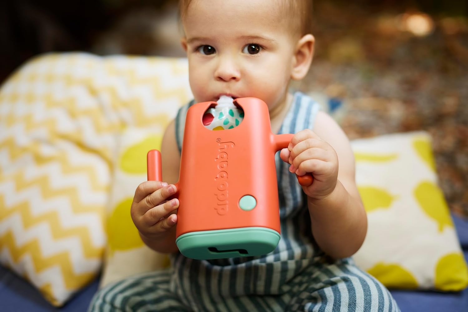 Criança com brinquedo laranja e verde sentada em almofadas com padrões amarelos e brancos