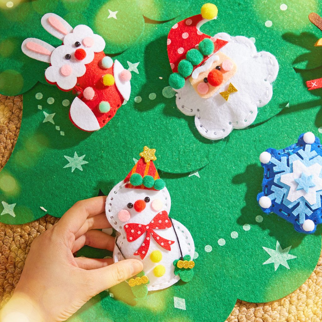 Bonecos de Natal em feltro colorido com pompons sobre base verde com estrelas e pontos brancos