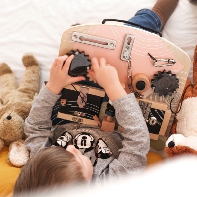 Criança a brincar num tabuleiro de atividades em madeira com peluches numa cama