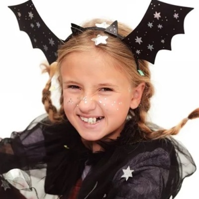 Menina com fantasia preta de morcego e tiara com asas decoradas com estrelas
