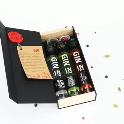 Conjunto de três frascos de gin numa caixa preta com cartão informativo e especiarias ao redor