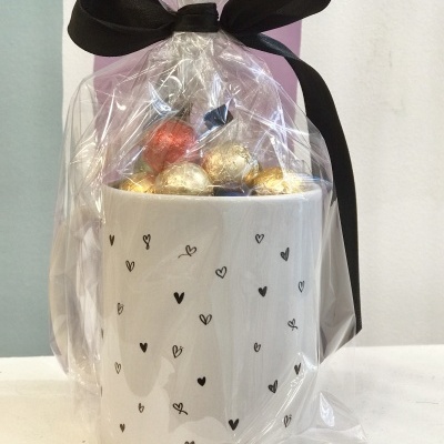 Caneca branca decorada com corações e chocolates embrulhados em celofane com laço preto