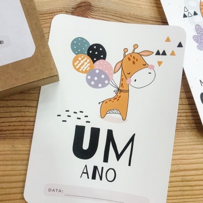 Cartão com girafa, balões e texto UM ANO sobre mesa de madeira