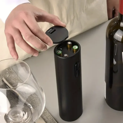 Dispositivo carregador preto com pilhas AA ao lado de copo e garrafa de vinho