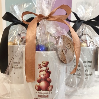 Canecas brancas com ilustração de ursinhos e texto, embaladas em plástico transparente com fitas, em fundo colorido.