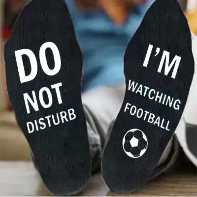 Meias pretas com texto branco 'DO NOT DISTURB' e 'I'M WATCHING FOOTBALL' com uma bola de futebol desenhada