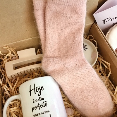 Meias rosas, caneca branca com texto em português e presilha bege numa caixa de presente.