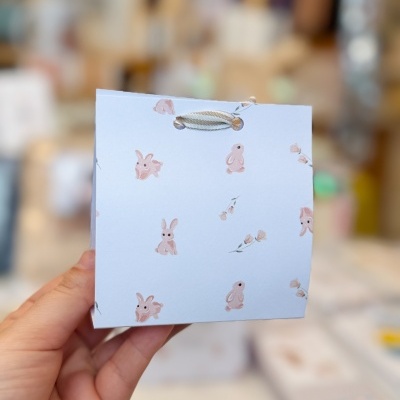 Saco de papel azul com padrão de coelhos cor-de-rosa e cordão branco