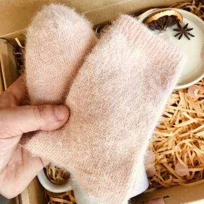 Par de luvas sem dedos cor bege claro em caixa com aparas de madeira e vela decorativa