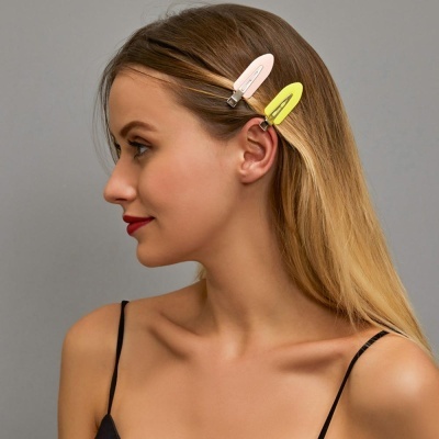 Dois ganchos de cabelo em tecido rosa e amarelo no cabelo de uma mulher loira com camisola preta