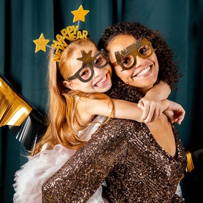 Duas raparigas com óculos de festa dourados 'HAPPY NEW YEAR' num ambiente festivo