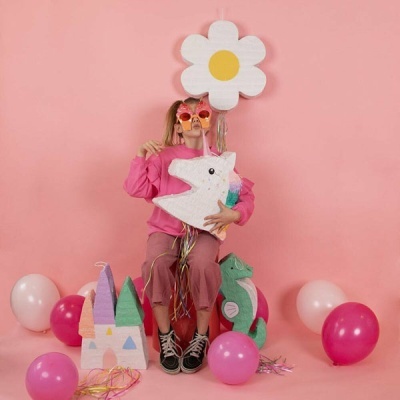 Criança com piñatas e balões num cenário cor-de-rosa