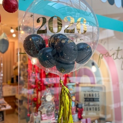 Balão transparente com bolas pretas e texto dourado 2026 em loja decorada