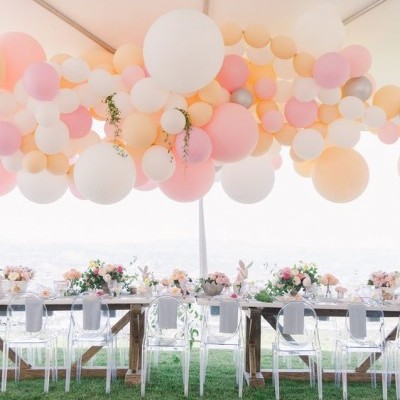 Decoração de festa com balões em tons pastel e mesas decoradas sob tenda