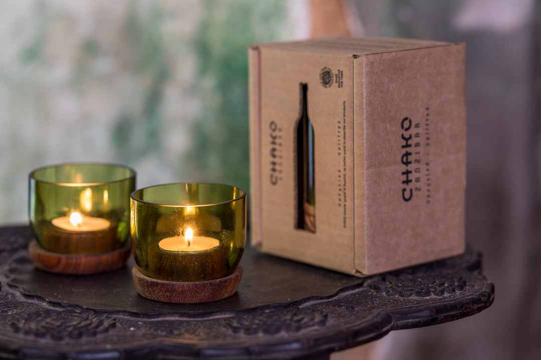 Suporte de vela Taa pequena Dois castiçais de vidro verde com base em madeira e uma caixa de embalagem castanha com o texto 'CHAKRA'.