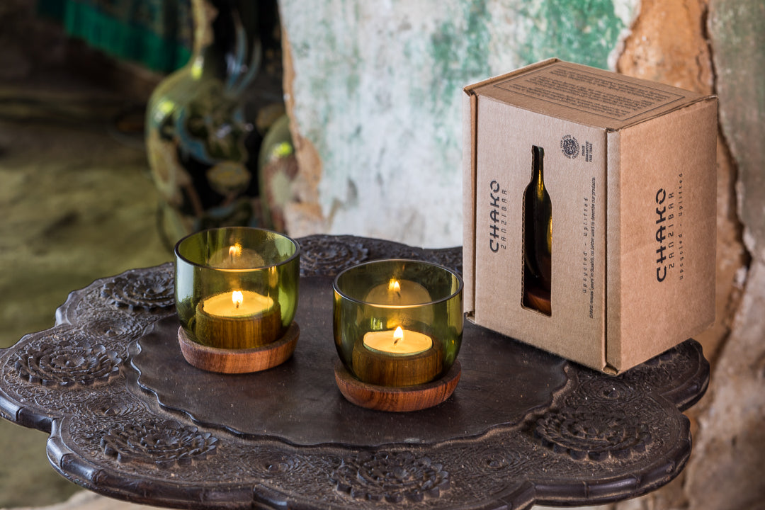 Suporte de vela Taa pequena Dois castiçais verdes com velas acesas e embalagem CHAIRO sobre mesa metálica escura