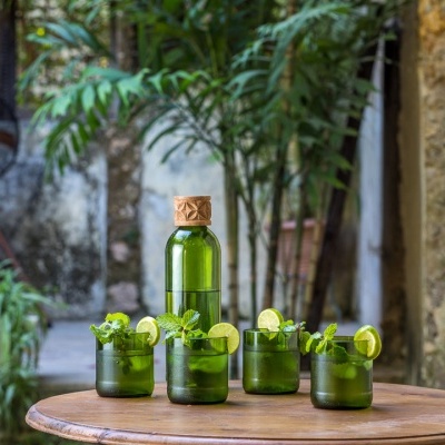 Garrafa e copos verdes com lima numa mesa redonda de madeira ao ar livre