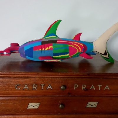 Escultura colorida de peixe sobre móvel de madeira com letras 'CARTA PRATA'