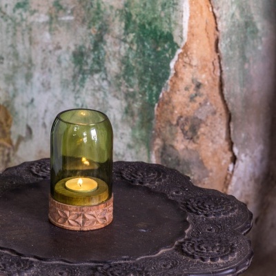 Vela em suporte de vidro verde sobre mesa preta com parede envelhecida ao fundo