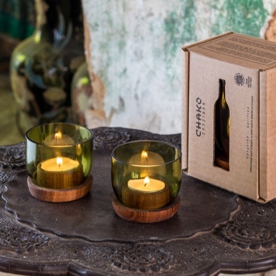 Dois castiçais verdes com velas acesas e embalagem CHAIRO sobre mesa metálica escura