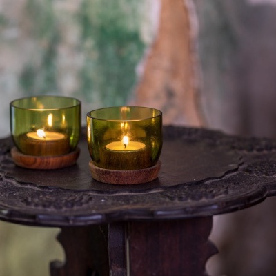 Duas velas verdes em copos de vidro com base de madeira numa mesa escura rústica