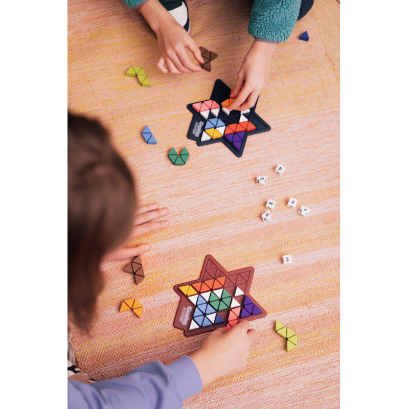 Crianças a jogar jogo de tabuleiro colorido em forma de estrela sobre tapete laranja.