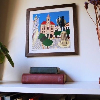 Quadro colorido com moldura castanha e dois livros sobre prateleira branca