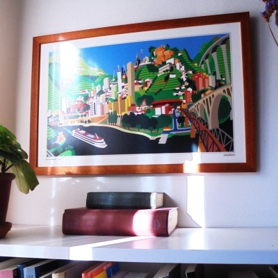 Quadro colorido com paisagem urbana sobre estante branca com livros e planta