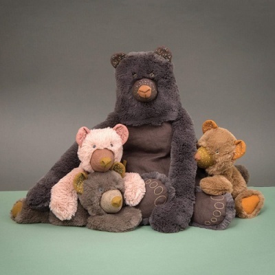 Quatro ursos de peluche de várias cores e tamanhos sobre superfície verde com fundo cinzento.