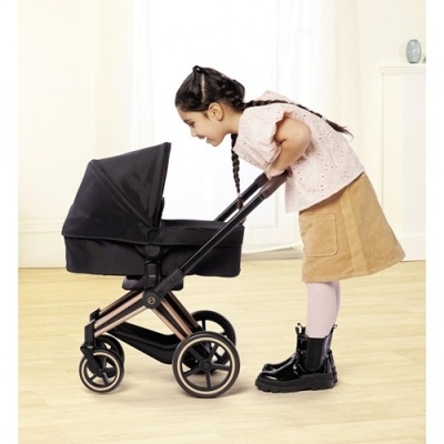 Criança a olhar para dentro de um carrinho de bonecas preto com estrutura metálica bronze