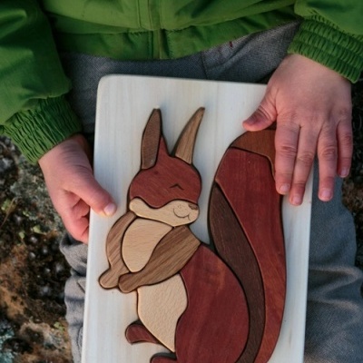 Quebra-cabeça de madeira em forma de esquilo com várias peças coloridas, segurado por criança com roupa verde e cinza.