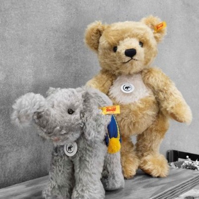 Urso e elefante de peluche em mesa de madeira com parede cinzenta ao fundo