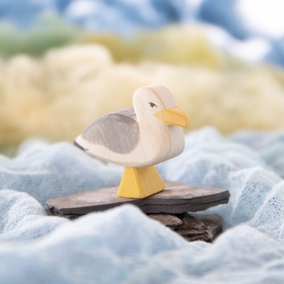 Figura de gaivota em madeira com cores naturais sobre tecido azul.