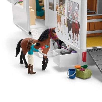 Boneco a dar banho a cavalo castanho junto a trailer branco com imagens de cavaleiros